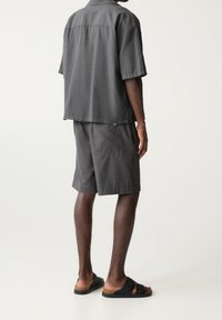 Camisa corta de color gris oscuro combinada con pantalones cortos a juego, con un corte relajado y tejido texturizado. Sandalias negras con dos correas.