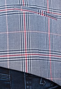Marynarka w kratę, w niebiesko-biało-czerwonej kolorystyce, z teksturowanej tkaniny. Zawiera detal w postaci kieszeni na piersi i jest nałożona na ciemne dżinsy.