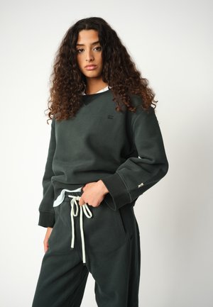 Felpa verde scuro con scollo a girocollo e polsini a coste, abbinata a pantaloni coordinati con coulisse e tasche laterali.