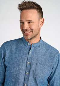 Camicia blu in chambray con colletto alla coreana, chiusura frontale con bottoni e taschino sul petto. Tessuto morbido, fantasie delicate e bottoni metallici.
