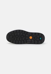 Semelle de chaussure en caoutchouc noir avec des crampons profonds pour l'adhérence, avec un logo circulaire orange et un petit hexagone turquoise près du talon.