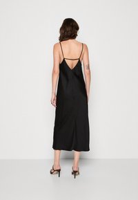 Robe de nuit en satin noir avec de fines bretelles, décolleté en V dans le dos, et silhouette longue jusqu'au sol. Présente une texture lisse et un style minimaliste.