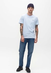 Svetlomodré bavlnené tričko s krátkymi rukávmi, s čiernym logom. Nosené so džínsami s rovnými nohavicami a čiernymi topánkami.