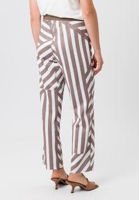Pantalons rayés marron et blanc avec une coupe slim, dotés d'une taille élastique et d'une texture lisse. Le design présente un détail d'ourlet fendu au niveau des chevilles.