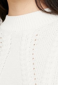 White knitted sweater featuring a ribbed neckline, textured cable patterns, and openwork details, creating a lightweight and breathable fabric.