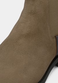 Bottine en suede marron avec une texture lisse, bout arrondi et une semelle foncée contrastante. Dispose de panneaux latéraux en élastique pour un enfilage facile.