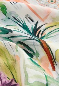 Close-up of sheer fabric with colorful abstract botanical print in green, orange, purple, and peach tones.