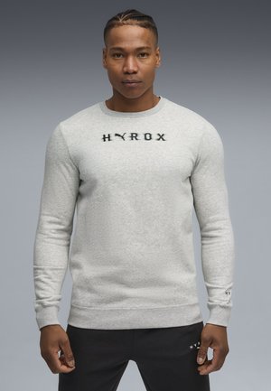 Grå bomulds sweatshirt med lange ærmer, rund halsudskæring, tekstureret stof, med sort "HYROX" logo hen over brystet og detaljer ved ærmerne.