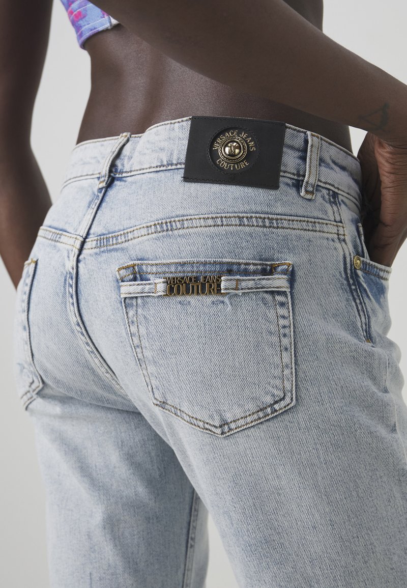 Jasnoniebieskie, biodrówki z denimu o wysokim stanie z teksturowanym wykończeniem. Zawierają złotą biżuterię "VERSACE JEANS COUTURE" i czarną skórzaną naszywkę z logo.