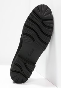 Svart gummiyttersula med ett strukturerat, vågigt mönster och en lätt upphöjd sektion vid hälen. Gabor-logotypen är präglad på sulan.