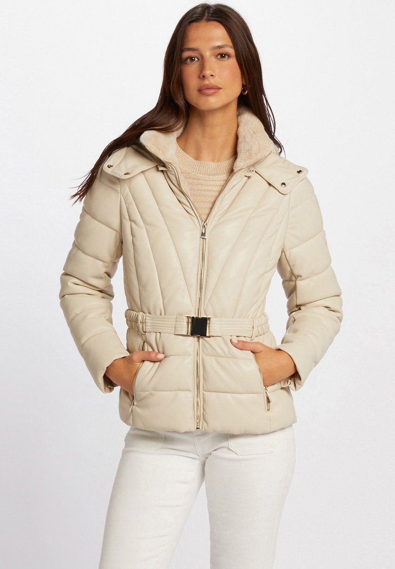 Giacca puffer beige con cintura in vita, chiusura zip e colletto in pelliccia sintetica. Presenta una texture trapuntata e tasche laterali. Accentuata da hardware dorato.