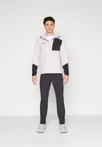 Ανοιχτό γκρι πλεκτή μπλούζα με μαύρη τσέπη στο στήθος και φερμουάρ· συνδυασμένο με μαύρο παντελόνι και ανοιχτό γκρι παπούτσια. Λείο υλικό, αθλητική εφαρμογή.