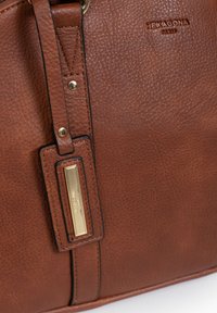 Borsa in pelle marrone con texture e accessori in metallo dorato. Presenta un'etichetta di marca prominente e attacchi per la tracolla robusti.