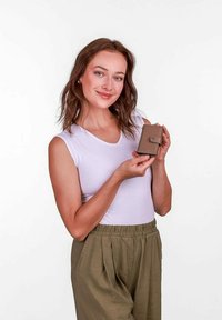 Hnědá kožená peněženka s klipem, která se vyznačuje kompaktním designem a viditelným šitím. Modelka má na sobě bílé tričko a olivové kalhoty.