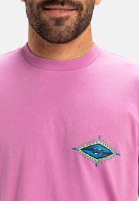 Majica kratkih rukava ružičaste boje od pamuka s grafičkim logotipom u plavoj i zelenoj boji, koja sadrži dijamantni oblik s dekorativnim akcentima.