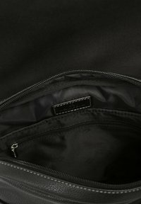 Interno di una borsa in pelle nera con una fodera morbida e testurizzata, dotata di una tasca con zip e un'etichetta di branding discreta.