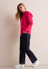 Sudadera fucsia con cordón, combinada con unos pantalones vaqueros de pierna ancha azul oscuro y zapatillas blancas, con una textura suave y un diseño casual.