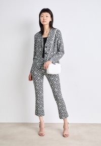Maßgeschneiderte Schwarz-Weiß-musterte Blazer und Hose, taillierte Silhouette, kombiniert mit einem schwarzen Oberteil und einer weißen Umhängetasche. Sichtbare leichte Absätze.