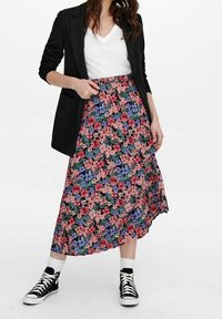 Gonna floreale con sfondo rosa, fiori blu e rossi, design a vita alta, materiale fluido, abbinata a un blazer nero e sneakers.
