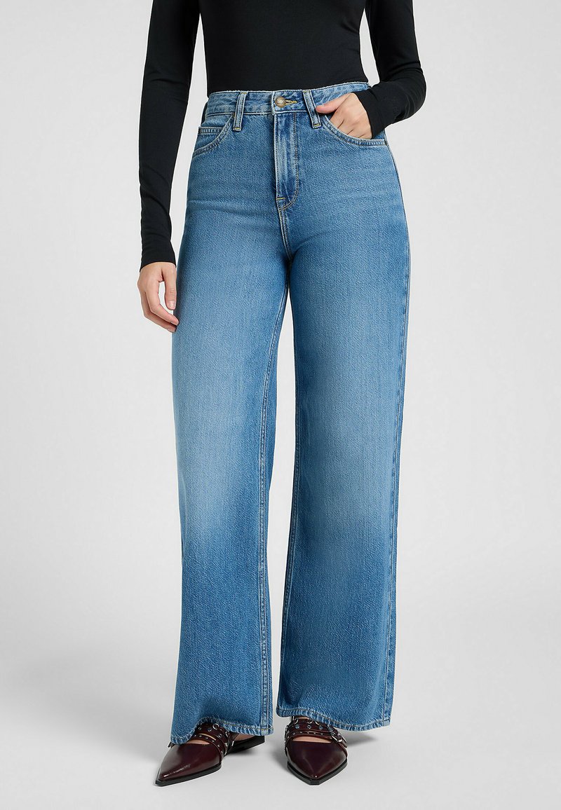 Høyt midje, vide jeans i lys blå denim. Har frontlommer og en lett falming. Brukt med spiss-tå, burgunder sko.
