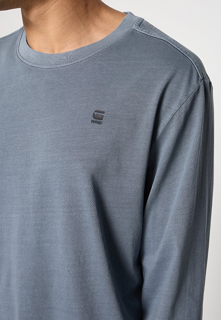 Langarmhemd in gedämpftem Blau, aus weichem Baumwollstoff. Verfügt über einen runden Halsausschnitt und ein kleines, dunkelgraues Logo auf der Brust.