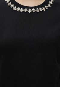 Haut noir avec un col rond orné d'une rangée décorative de strass clairs en forme ovale et de petits cristaux ronds.