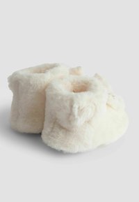 Vita plyschtofflor med en mjuk, fluffig textur, som har en rund form och design med vikbar mudd. Försedda med små dekorativa detaljer.
