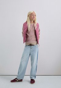 Chaleco acolchado rosa sobre un suéter de rayas beige, combinado con jeans anchos de un azul claro con una franja azul y zapatillas burdeos.