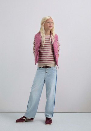 Chaleco acolchado rosa sobre un suéter de rayas beige, combinado con jeans anchos de un azul claro con una franja azul y zapatillas burdeos.