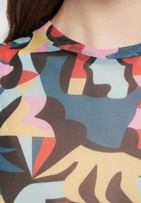 Haut en maille colorée présentant un motif abstrait dans des nuances de bleu, rouge, rose et beige, avec un col arrondi et une texture légère.