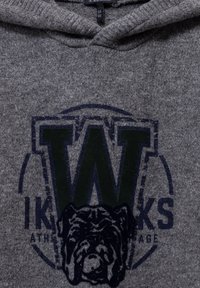 Sudadera gris con un logo redondo que presenta una gran letra "W" en verde. Incluye un gráfico de bulldog, fabricado con un material suave y texturizado.