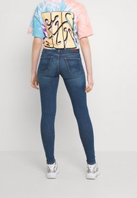 Vaqueros ajustados de mezclilla azul desgastada con dos bolsillos traseros. Combinados con una camiseta de manga corta de tintes anudados que presenta un gran texto gráfico.