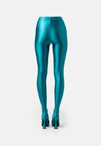 Leggings lucidi in teal con un design elegante e una silhouette aderente, caratterizzati da vita alta e lunghezza alla caviglia estesa, abbinati a tacchi a spillo.