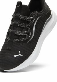 Sneaker nera Puma con suola bianca, dettagli riflettenti e lacci a pois neri e bianchi, con il logo Puma sulla punta.