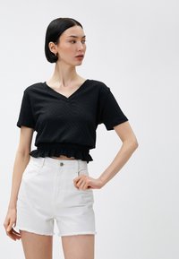 Sort cropped top med V-hals og korte ærmer, der har et tekstureret stof og en flæsekant. Kombineret med hvide shorts med høj talje.