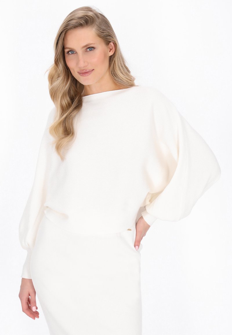 Pull en tricot blanc à côtes avec un large col bateau et des manches oversize, associé à une jupe ajustée assortie. Texture lisse, design minimaliste.