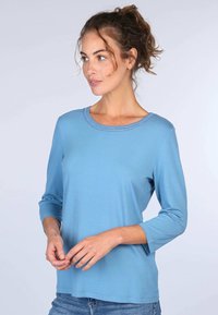 Hellblaue Langarmbluse mit rundem Ausschnitt und dekorativen Nähten. Glattes Material mit lockerer Passform, ideal für Freizeitbekleidung.