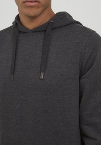 Dark gray hoodie made of soft fabric, featuring a drawstring hood with metal tips and a front pocket. The texture appears smooth and casual.