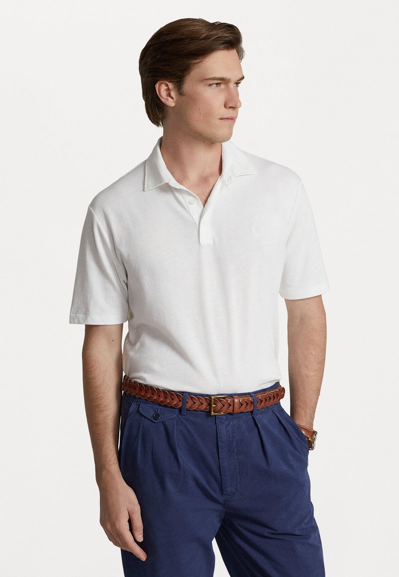 Witte polo met korte mouwen, met een kraag en een knoopsluiting met twee knopen, gecombineerd met marineblauwe broek en een bruine gevlochten riem.