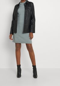 Czarna skórzana kurtka na jasnoszarym dzianinowym sukience z prążkowanym wykończeniem, zestawiona z czarnymi botkami za kostkę. Gładka faktura i dopasowany krój.