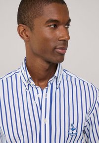 Camisa de manga larga a rayas azul y blanca con cuello, que presenta un pequeño logo bordado en el lado izquierdo. Tejido de algodón, corte casual.
