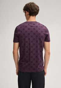 Lila T-Shirt mit kurzen Ärmeln, das ein strukturiertes Muster aufweist, runden Ausschnitt und einen leicht taillierten Schnitt hat. Der Stoff wirkt glatt und leicht.