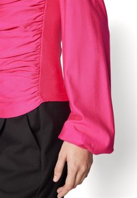 Tight passande topp i en livlig rosa färg, rynkad struktur på ena sidan och slät ärm. Stylistisk med svarta skräddarsydda byxor.