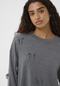 Gray sweater made of soft material featuring decorative fabric bows, wide sleeves, and a ribbed neckline, with a relaxed fit.