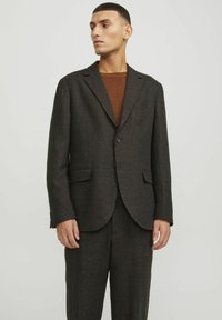 Blazer in tweed marrone con superficie texturizzata, rever a punta, chiusura con un pulsante e due tasche frontali, indossato sopra un top in maglia marrone.