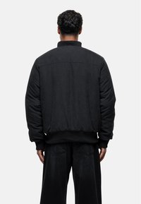 Giubbotto bomber nero con una texture liscia, caratterizzato da un alto colletto, polsini e orlo a coste, e un design del pannello posteriore cucito.