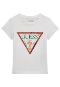 Valkoinen puuvillapaita, jossa on suuri kolmionmuotoinen logo paljeteista vihreillä ja punaisilla yksityiskohdilla, sekä "GUESS U.S.A." -teksti sisällä.