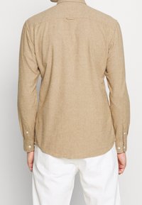 Beige Langarmshirt aus strukturiertem Stoff; mit Knopfmanschetten und abgerundetem Saum. Die Rückansicht zeigt Kragen und Nahtdetails.