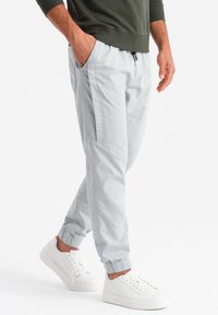 Pantalones jogger ajustados de color gris claro con puños elásticos y bolsillos laterales, combinados con zapatillas blancas. Tejido suave con una textura lisa.