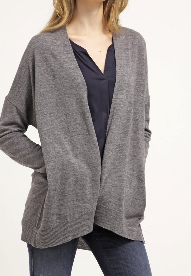 Cárdigan gris de manga larga hecho de un tejido suave, con un frente abierto, que presenta un corte relajado y un dobladillo acanalado. Combinado con una parte superior oscura y jeans.